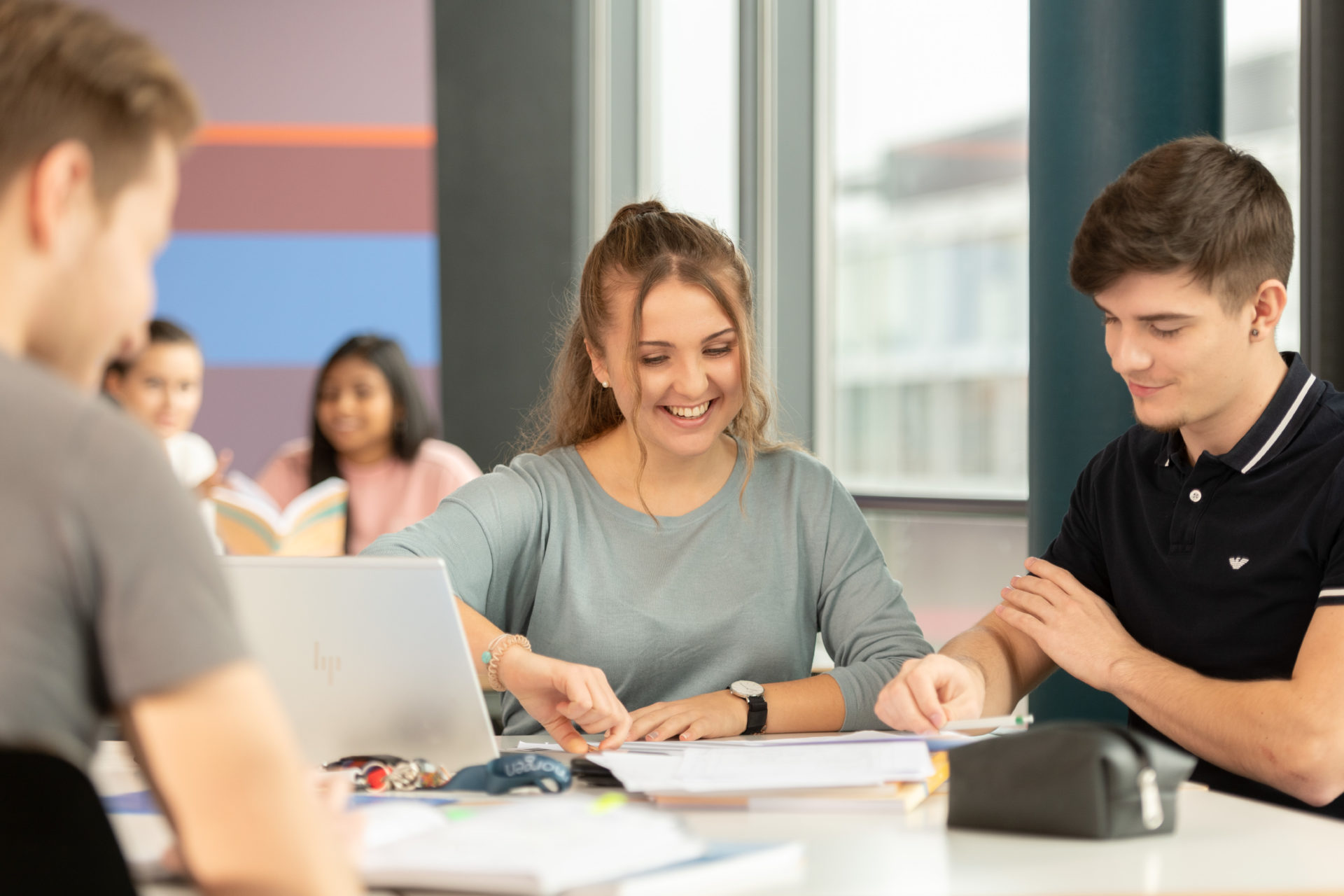 Lernende um ein Pult herum platziert, die auf Aufgaben-Blätter schauen.
