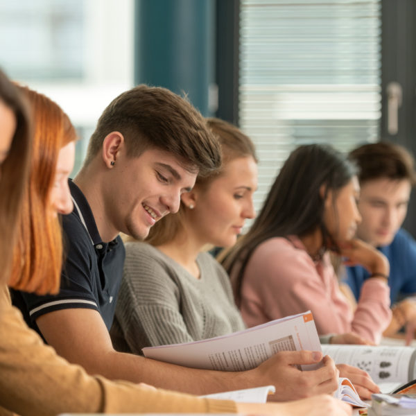Sieben Lernende im Klassnzimmer, am Pult sitzen und in die Lernbücher schauen.
