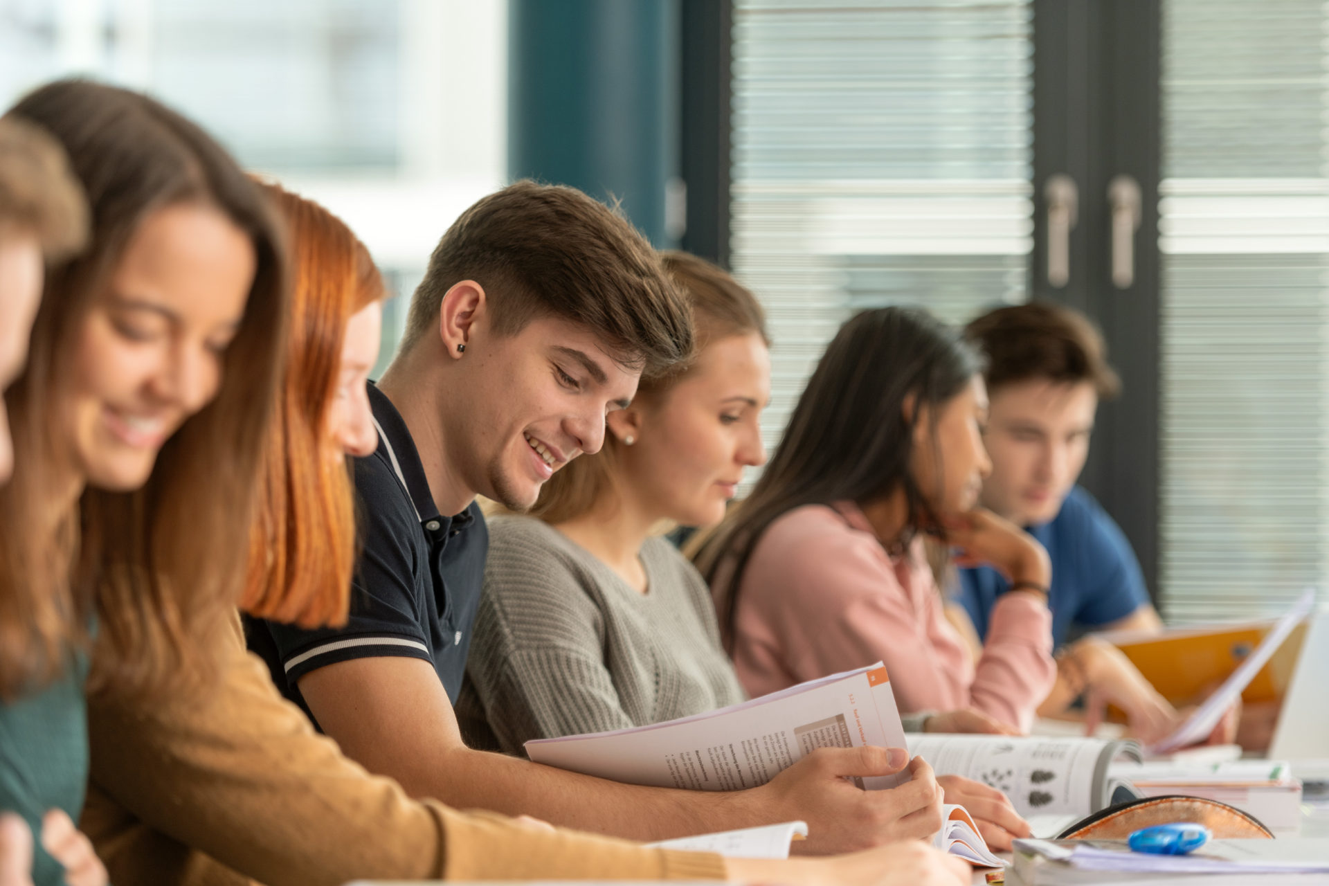 Sieben Lernende im Klassnzimmer, am Pult sitzen und in die Lernbücher schauen.