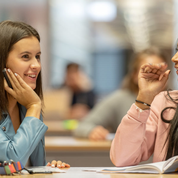 Zwei Lernende, die im Gang vor den Klassenzimmer stehen und in ein Buch schauen.