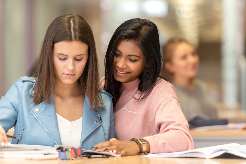 Zwei Lernende, die im Gang vor den Klassenzimmer stehen und in ein Buch schauen.