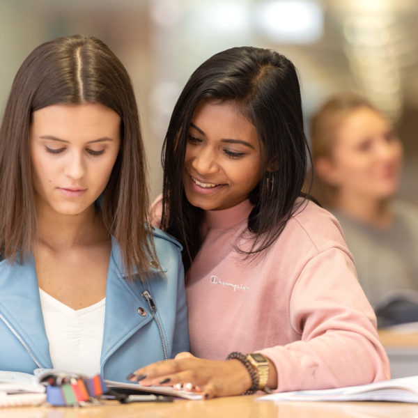 Zwei Lernende, die im Gang vor den Klassenzimmer stehen und in ein Buch schauen.