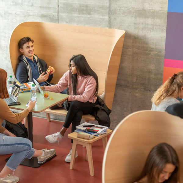 Lernende in der Pause auf verschiedene Ohrsessel aus Holz sitzend.