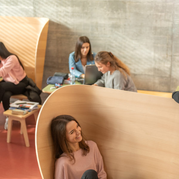 Lernende in der Pause auf verschiedene Ohrsessel aus Holz sitzend.