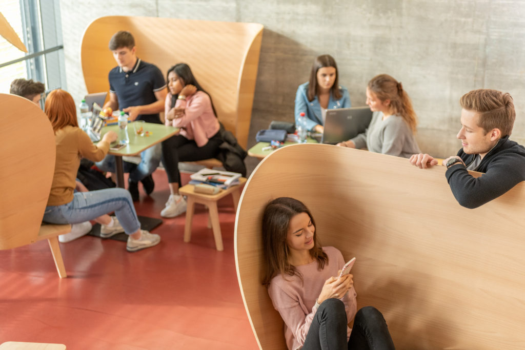 Lernende in der Pause auf verschiedene Ohrsessel aus Holz sitzend.