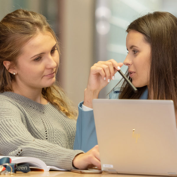 Zwei Lernende vor einem Laptop am diskutieren im Gang des bwd Schulgebäudes