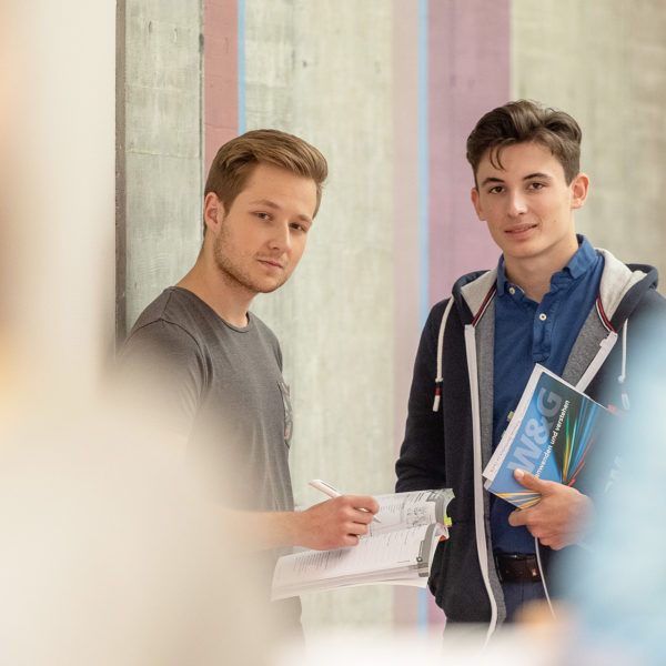 Zwei Lernende im Gang stehend mit Bücher in den Händen.