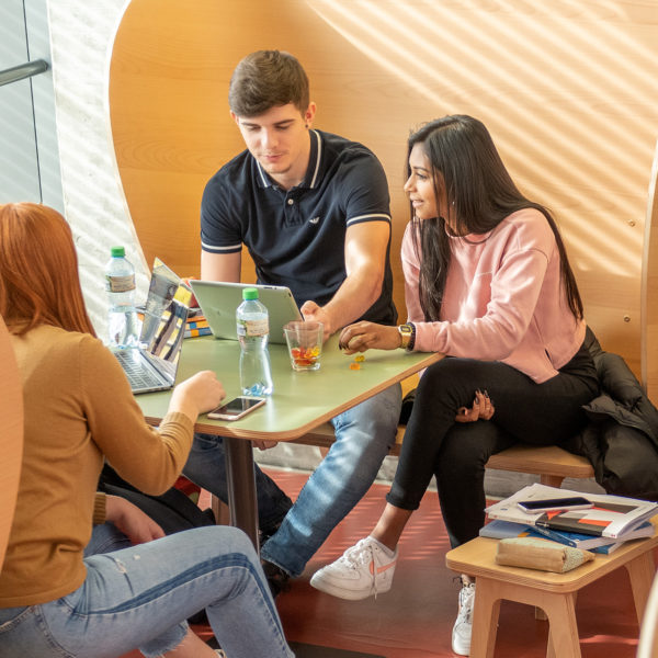 Vier Lernende der bwd Bern rund um einen Tisch auf Holz-Ohrsessel sitzend.