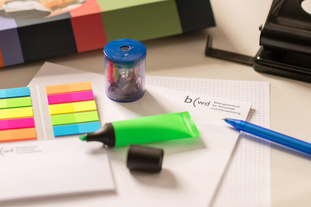 Nahaufnahme von Schreibblock, Kugelschreiber, Bleistift, Radiergummi ,Merkkleber, Leuchtstift, Spitzer. Durcheinander aufs Pult gelegt.