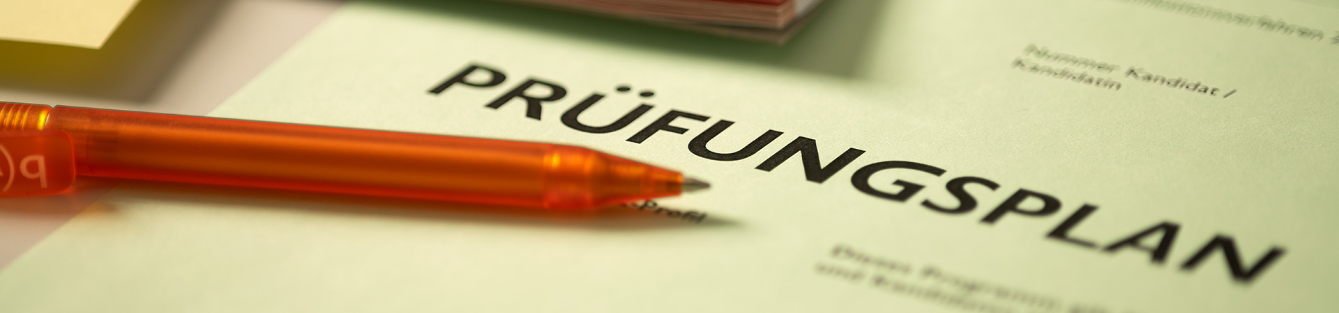 Prüfungsplan Titel in Nahaufnahme. Darüber ist ein oranger bwd Kugelschreiber.