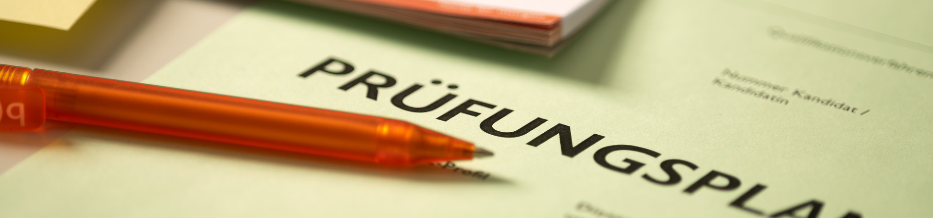 Prüfungsplan Titel in Nahaufnahme. Darüber ist ein oranger bwd Kugelschreiber.