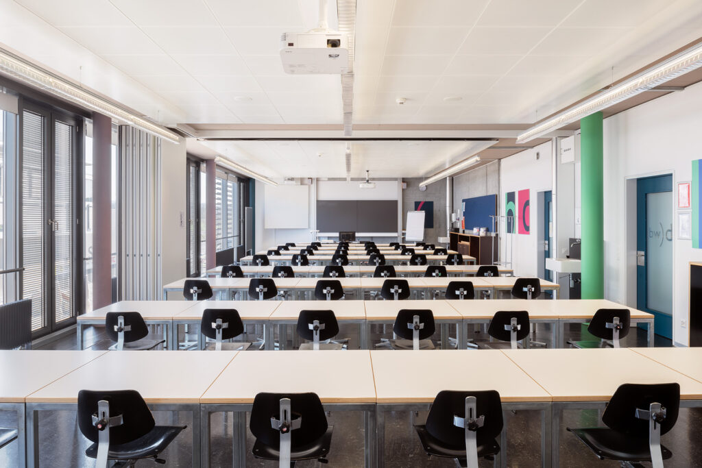 Klassenzimmer 310 und 311 zusammengelegt. 8 Reihen à 6 Stühle. Wandtafel, Beamer und Leinwand sind ersichtlich.